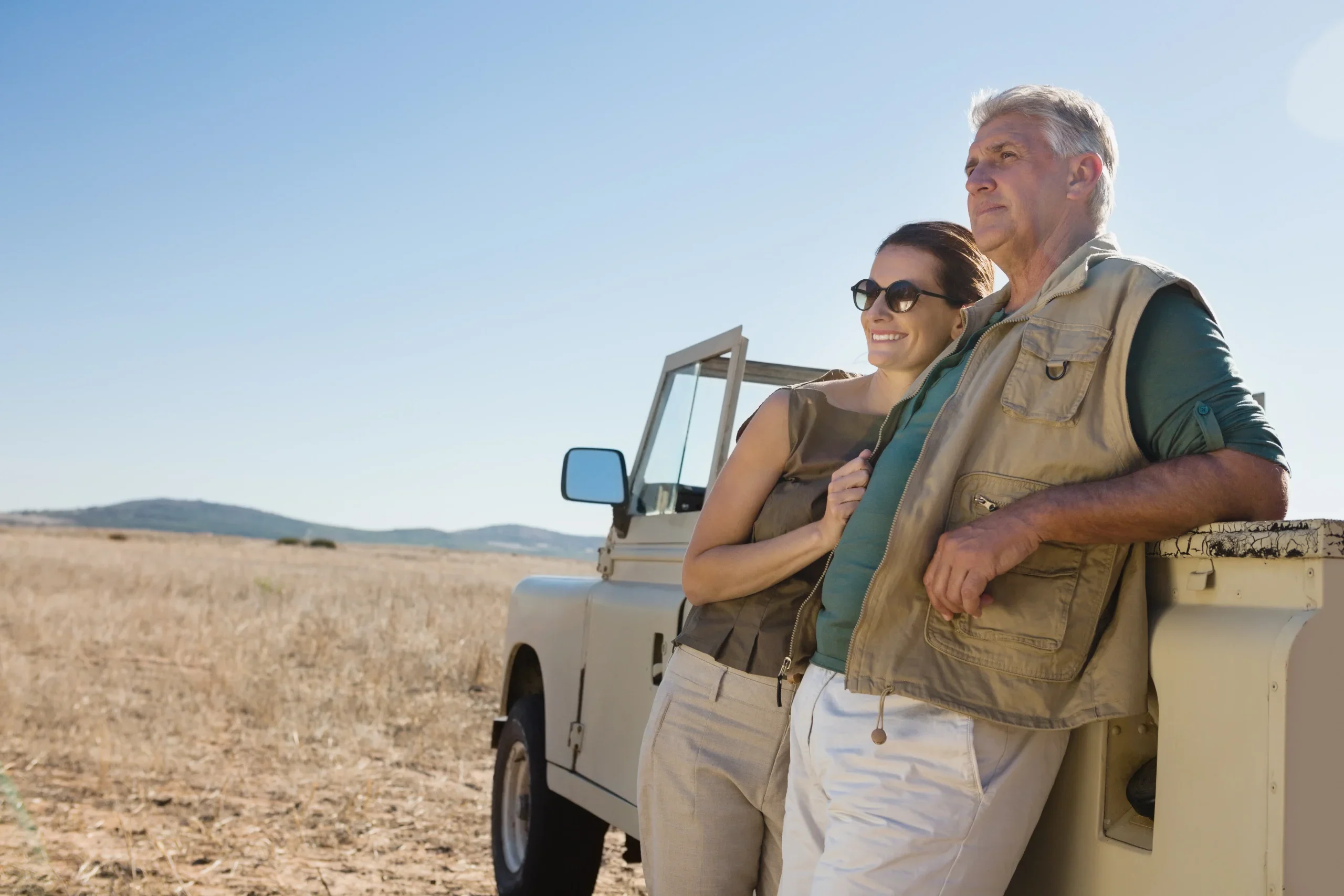 couple-looking-away-while-standing-by-vehicle-field