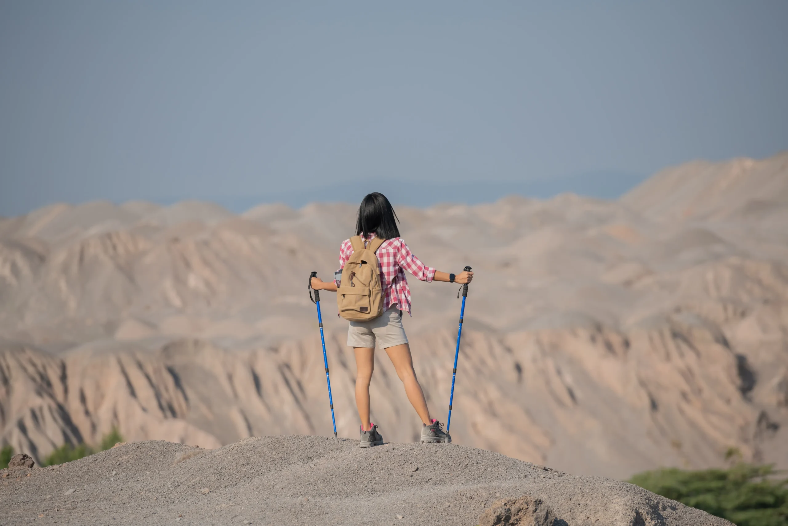 fit-young-woman-hiking-mountains-standing-rocky-summit-ridge-with-backpack-pole-looking-out-landscape